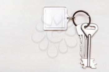 bunch of keys on keyring with blank white keychain on pale brown table
