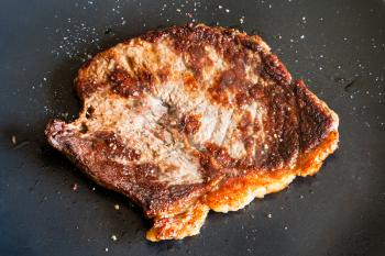 piece of roasted meat sprinkled with pepper and salt on black plate