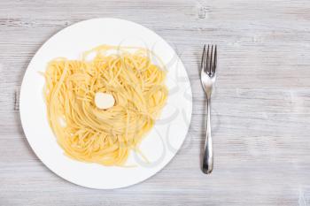 italian cuisine - top view of spaghetti al burro (pasta with butter) on white plate and fork on gray wooden table with blank copyspace