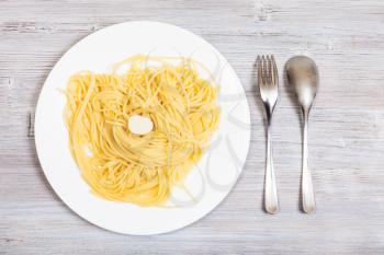 italian cuisine - top view of spaghetti al burro (pasta with butter) on white plate and fork wit spoon on gray wooden table