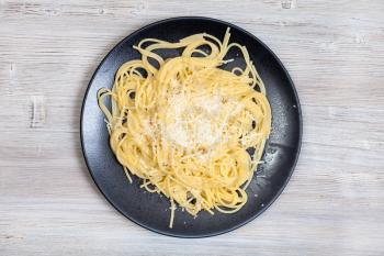 italian cuisine - top view of spaghetti al burro e parmigiano (pasta with butter and cheese) on black plate on gray wooden background