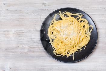 italian cuisine - top view of spaghetti al burro e parmigiano (pasta with butter and cheese) on black plate on gray wooden background with blank copyspace