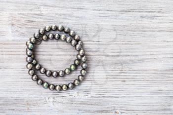 top view of coiled natural black pearls beads on gray wooden board with copyspace