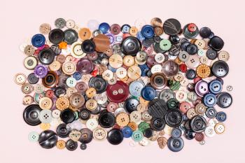 top view of pile of many various buttons on pink background