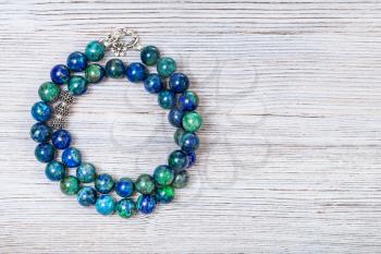 needlecraft background - handcrafted necklace from polished azurite gemstones on gray wooden board with copyspace