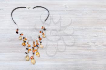 needlecraft background - top view of hand crafted necklace decorated by chains with natural citrine and cornelian gemstonesa and pearls red on gray wooden board with copyspace
