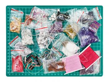 needlecraft background - top view of various items, beads, bugles, spangles, threads, gimps for embroidery on green cutting mat isolated on white background