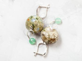 hand crafted silver earrings with rhyolite and nephrite beads on gray concrete background