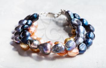 hand crafted bracelet from three stings of colored river pearls on gray concrete board