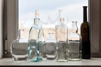 many empty drunk bottles on windowsill and view of city park through home window on sunny spring day on background
