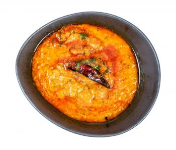 Indian cuisine - top view of portion of yellow Dal Tadka (spicy smooth and creamy chowder from lentils with curry) in black bowl isolated on white background