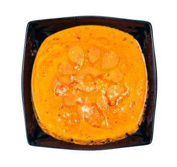 Indian cuisine - top view of portion of Chicken tikka masala (pieces of roasted marinated chicken in spicy curry creamy sauce) in black bowl isolated on white background
