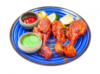 Indian cuisine - portion of Tandoori chicken (spicy chicken legs marinated in yogurt and spices and roasted in tandoor) with sauces on blue ceramic plate isolated on white background