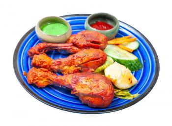 Indian cuisine - cooked Tandoori chicken (spicy chicken legs marinated in yogurt and spices and roasted in tandoor) with sauces on blue ceramic plate isolated on white background