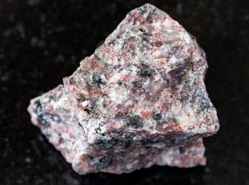 closeup of sample of natural mineral from geological collection - unpolished pink Granite rock on black granite background