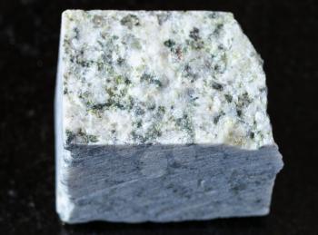 closeup of sample of natural mineral from geological collection - raw white Granite rock on black granite background