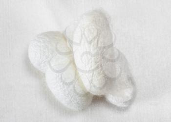 few organic silkworm cocoons for facial skin care on white silk fabric close up