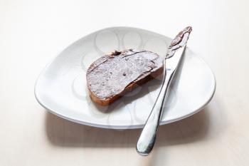 slice of bread with chocolatte and hazelnut spread and knife on plate on table