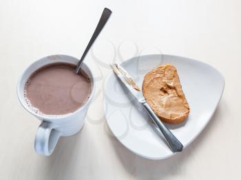 top view of cup with cocoa and toast with peanut butter on plate on table