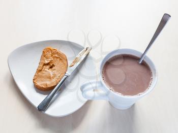 top view of mug with hot chocolatte and toast with peanut butter on plate on table