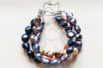 handcrafted bracelet from colored natural river pearls and silver clasp close up on pale wooden board