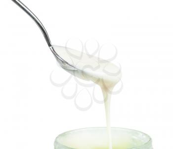 side view of natural organic white honey flows from steel spoon into glass jar close up isolated on white background