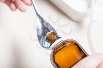 woman pours medicine from glass bottle into steel spoon close up