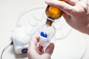 woman dripping inhalation solution from vial into nebulizer close up