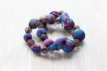 tangled handcrafted necklace of round beads wrapped in blue silk cloth and metal spiral beads on wooden table