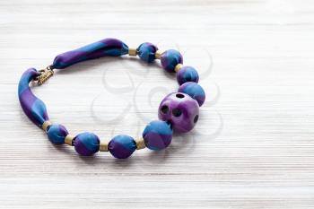 handcrafted necklace of round beads wrapped in blue silk cloth and purple plastic ball with holes on wooden table with copyspace