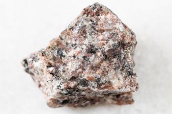 closeup of sample of natural mineral from geological collection - unpolished pink Granite rock on white marble background