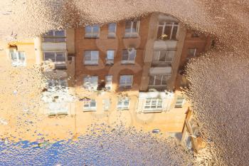 rain puddle with reflection of high-rise apartment house on surface of asphalt road in city on sunny autumn day