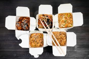 top view of chinese fast food in disposable cardboard boxes and wooden chopsticks on black table