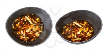 set of Chinese sour and hot spicy soup with shrimp and chicken (broth with chicken, shrimp, tofu, bamboo, mushrooms, egg and dark soy sauce) in black bowls isolated on white background