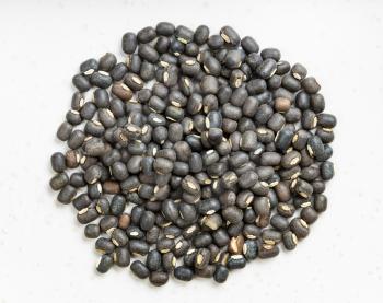 pile of raw whole black urad beans close up on gray ceramic plate