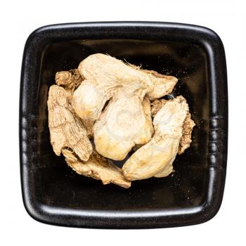 top view of dried pieces of ginger in black bowl isolated on white background
