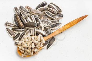 top view of cores in wood spoon and pile of sunflower seeds on gray ceramic plate