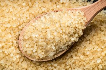above view of wooden spoon with demerara brown cane sugar close up on pile of sugar