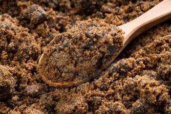 above view of wooden spoon with dark muscovado cane sugar close up on pile of sugar