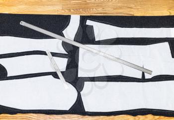 layout of sewing patterns of dress and steel rulers on dark fabric on wooden table