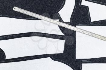 paper layout of sewing patterns of dress and steel ruler on dark fabric