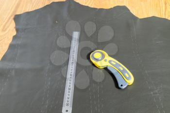 steel ruler and rotary cutter on leather with drawn pattern at wooden table