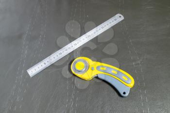 steel ruler and rotary cutter on surface of leather with drawn pattern