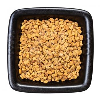 top view of whole fenugreek seeds in black bowl isolated on white background