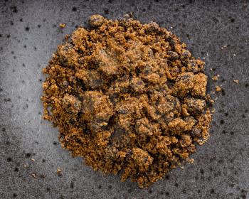 top view of pile of dark muscovado cane sugar close up on black ceramic plate