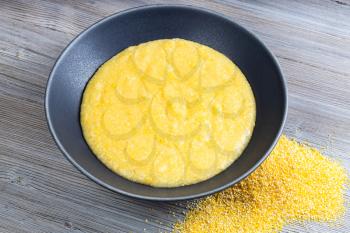 cooked maize porridge in gray bowl and handful of cornmeal on gray wooden table