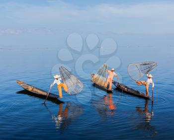 Myanmar travel attraction landmark - Traditional Burmese fishermen balancing with fishing net on boats at Inle lake in Myanmar famous for their distinctive one legged rowing style