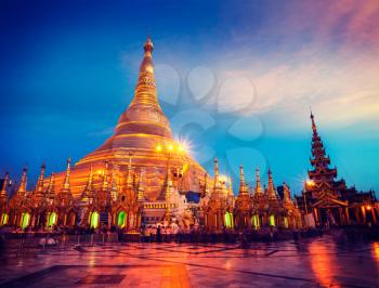 Vintage retro effect filtered hipster style image of Myanmer famous sacred place and tourist attraction landmark - Shwedagon Paya pagoda illuminated in the evening. Yangon, Myanmar Burma