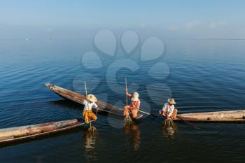Myanmar travel attraction landmark -  three traditional Burmese fishermen fishing on boats atInle lake in Myanmar famous for their distinctive one legged rowing style