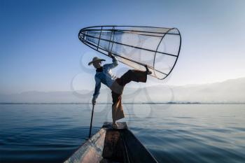 Myanmar travel attraction landmark - Traditional Burmese fisherman silhouette balancing with fishing net at Inle lake in Myanmar famous for their distinctive one legged rowing style, view from boat
